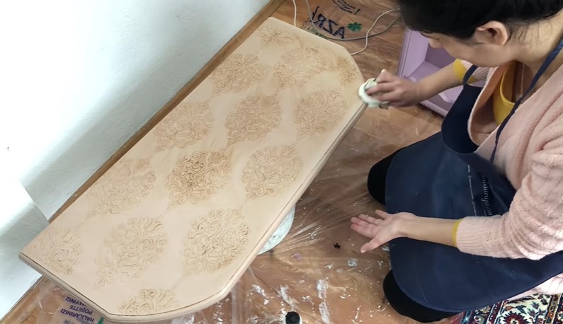Desenleri biraz daha ortaya çıkarmak ve eskitme görünümü vermek için, Sisal rengine boyadığımız yüzeyin üzerine eskitme kremi uyguluyoruz. Ürünü yüzeye gelişigüzel sürüyoruz. Ardından nemli bir bezle yüzeye silme işlemi uyguluyoruz.